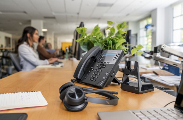 A Voyager 4300 UC stereo headset is placed next to a softphone and a base on a desk in the office.